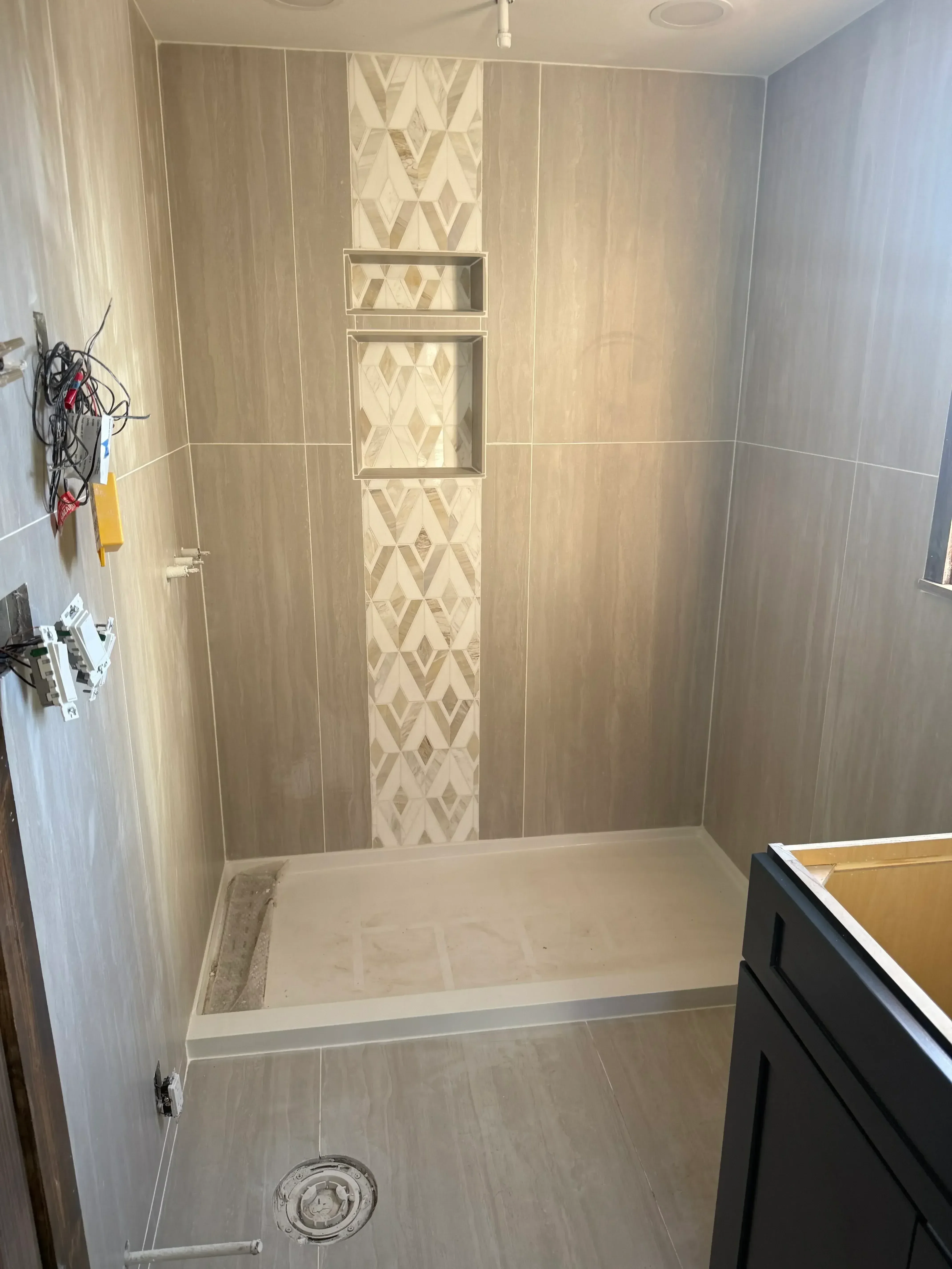 Bathroom shower with large-format gray porcelain tiles, geometric accent band, and recessed niches