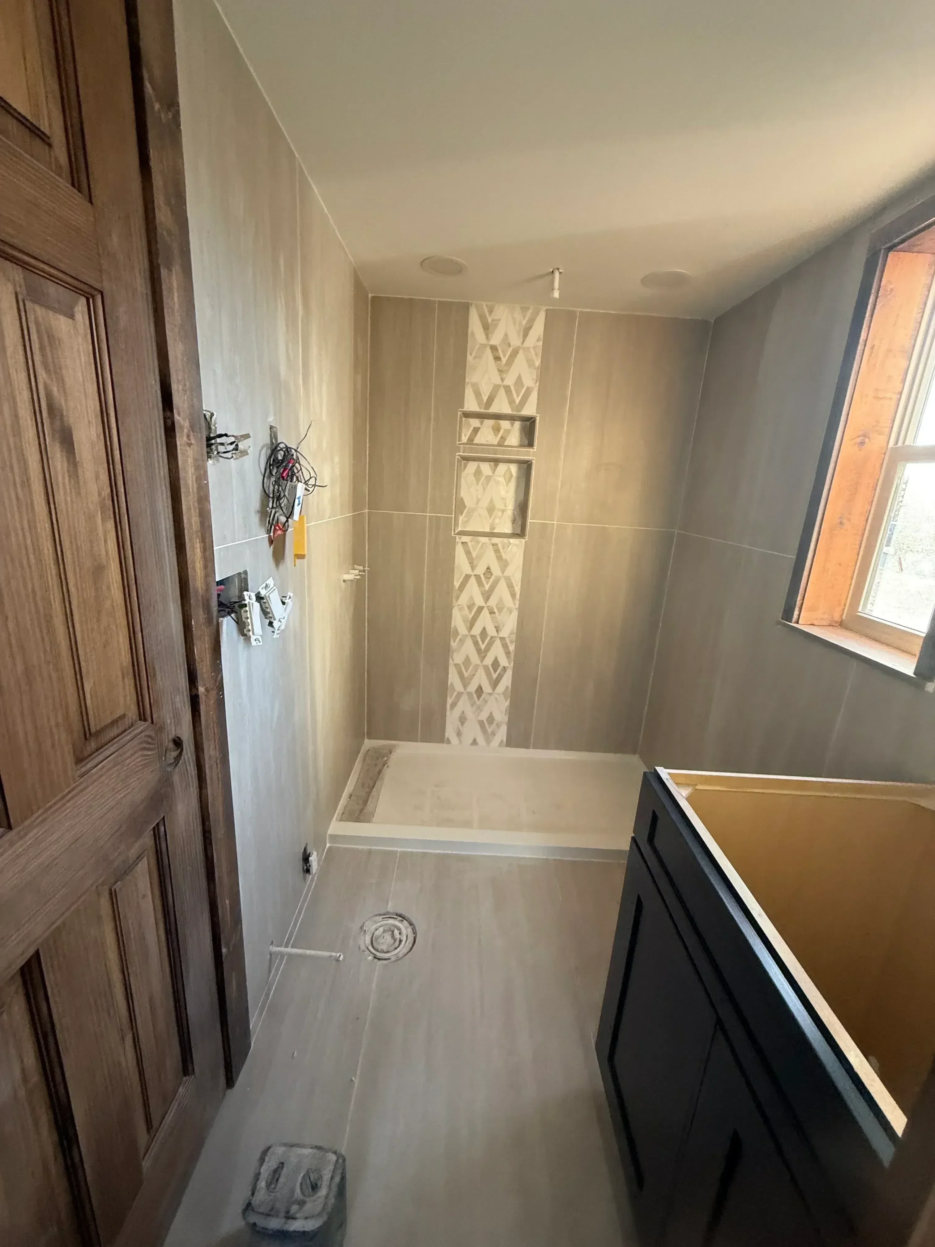 Bathroom shower area with large ceramic tile walls, geometric border strip, and dual niches during installation