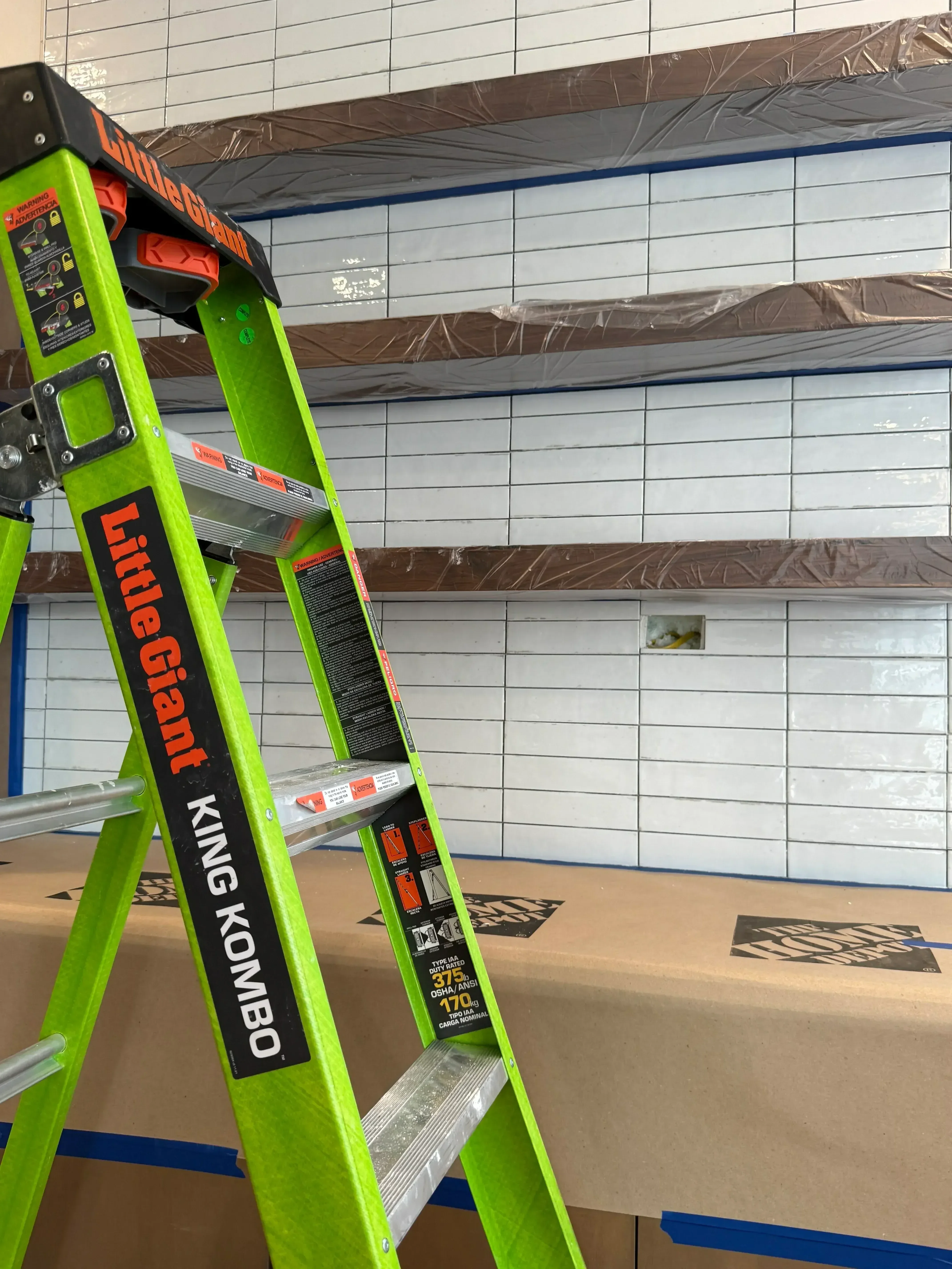 White subway tile backsplash installation with grout lines and protective coverings on adjacent walls