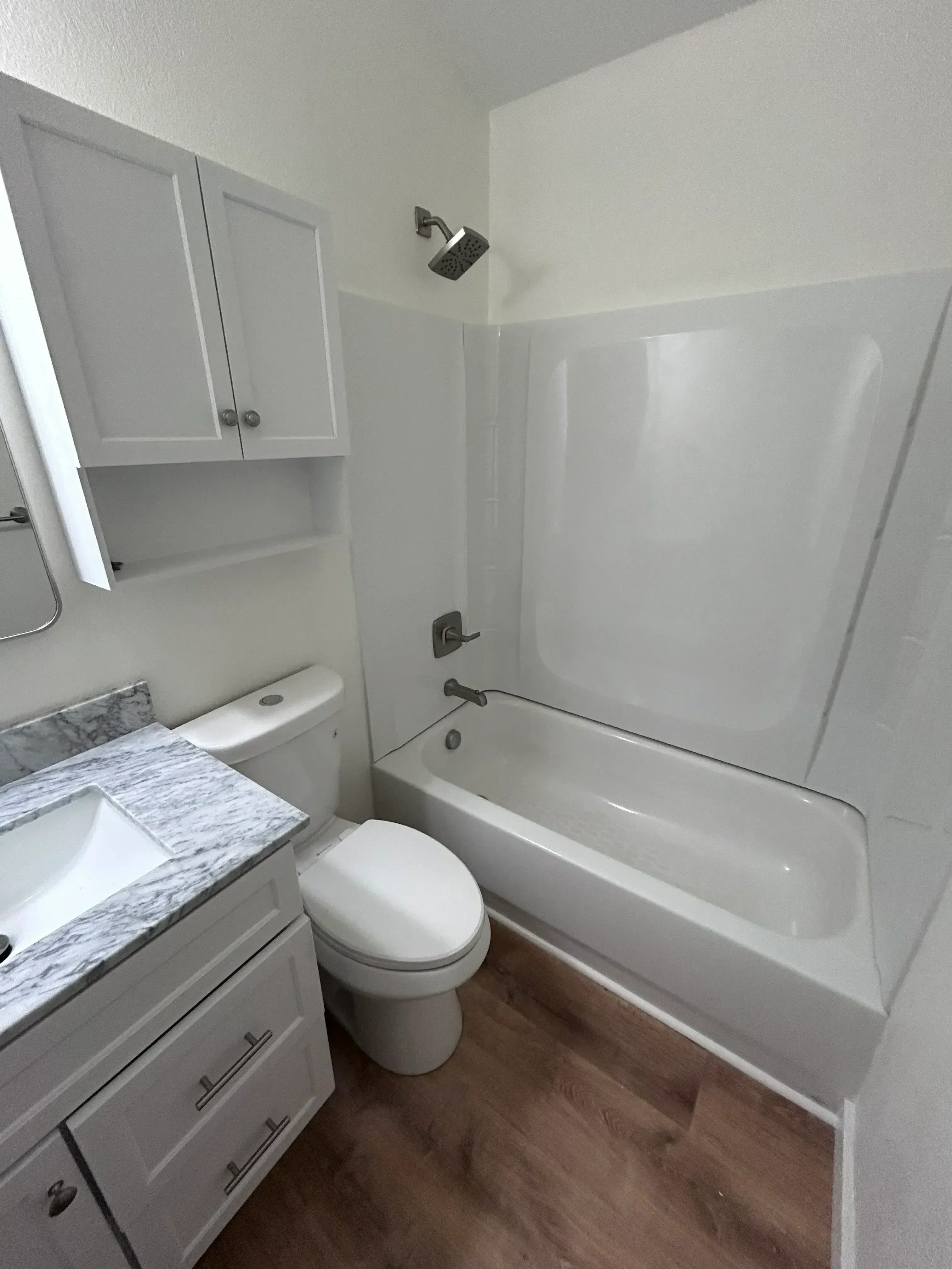 Newly installed white bathroom vanity with marble countertop, toilet, and recessed lighting