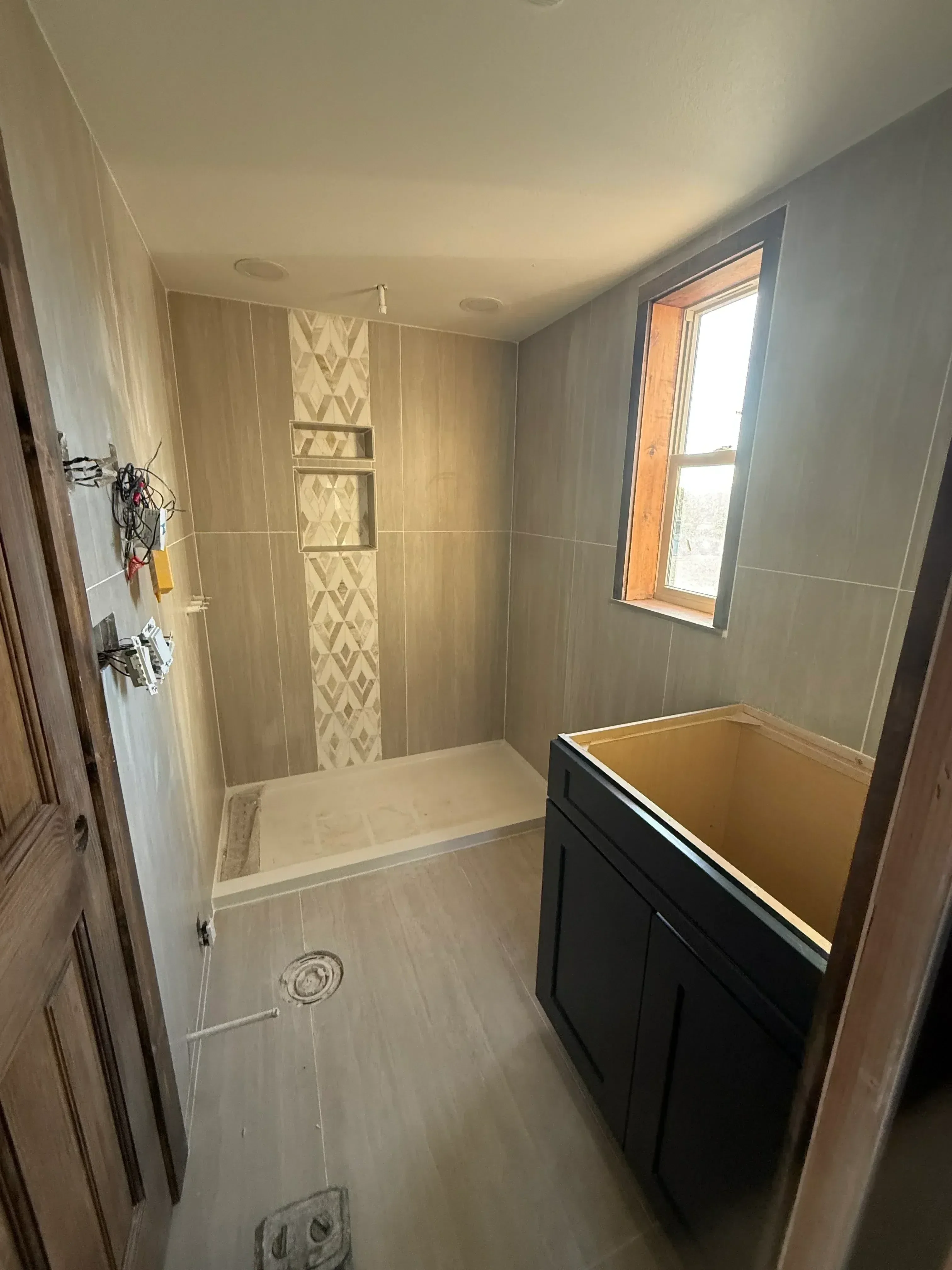 Bathroom shower with large-format porcelain tile walls, geometric accent band, and recessed lighting installation