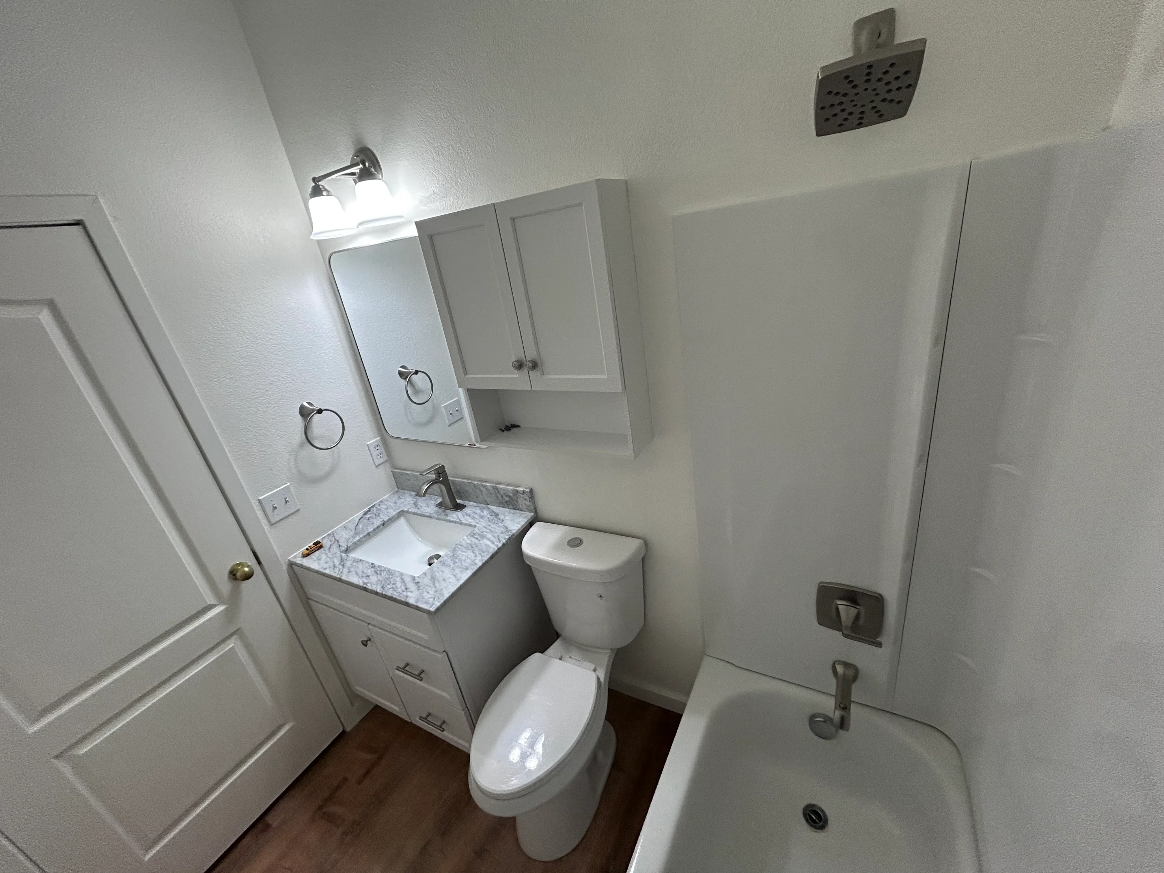 Renovated bathroom with marble vanity, white cabinetry, toilet, and rainfall showerhead