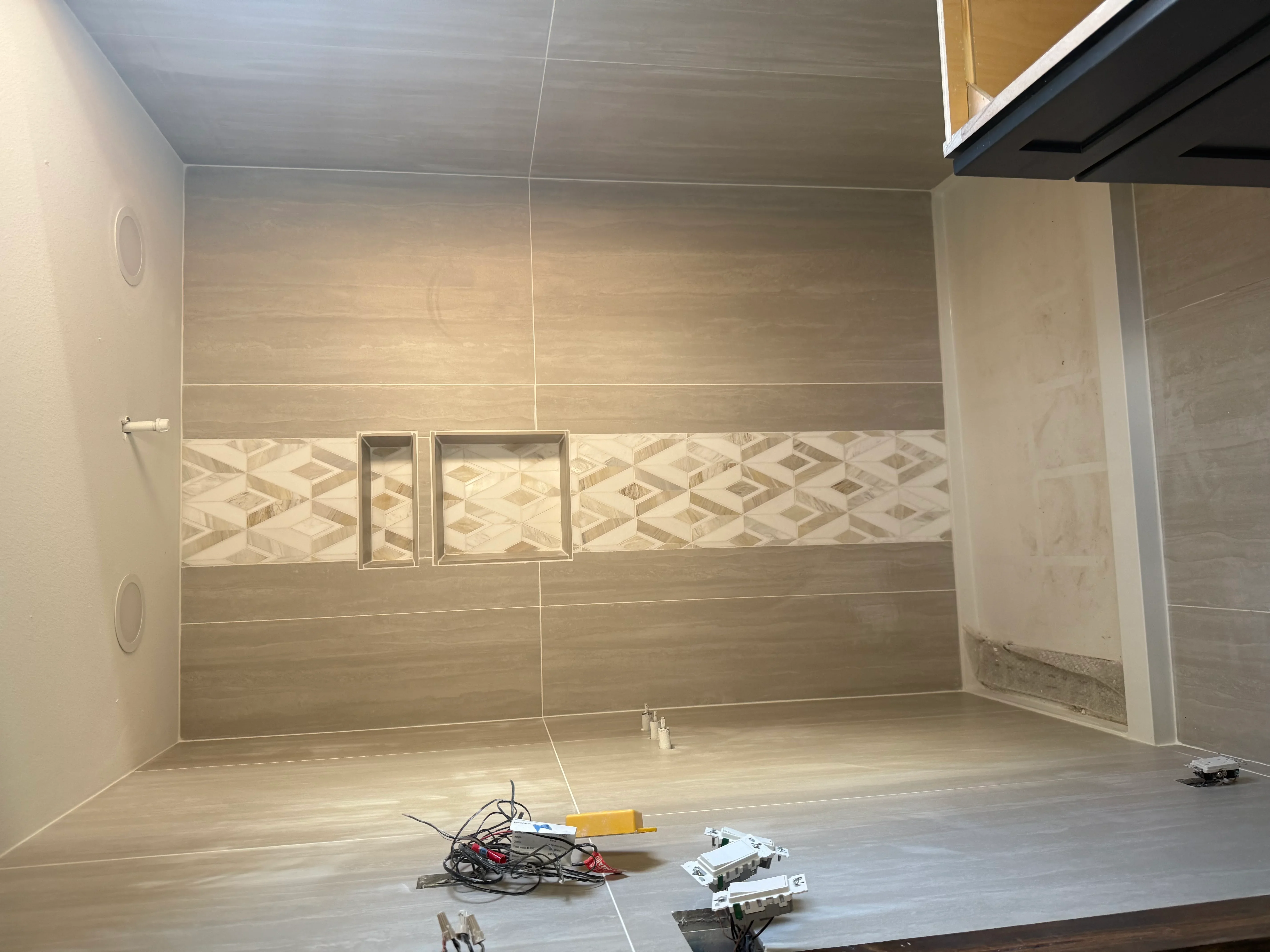 Walk-in shower with wood-tone tile, geometric accent band, and chrome recessed niches during installation