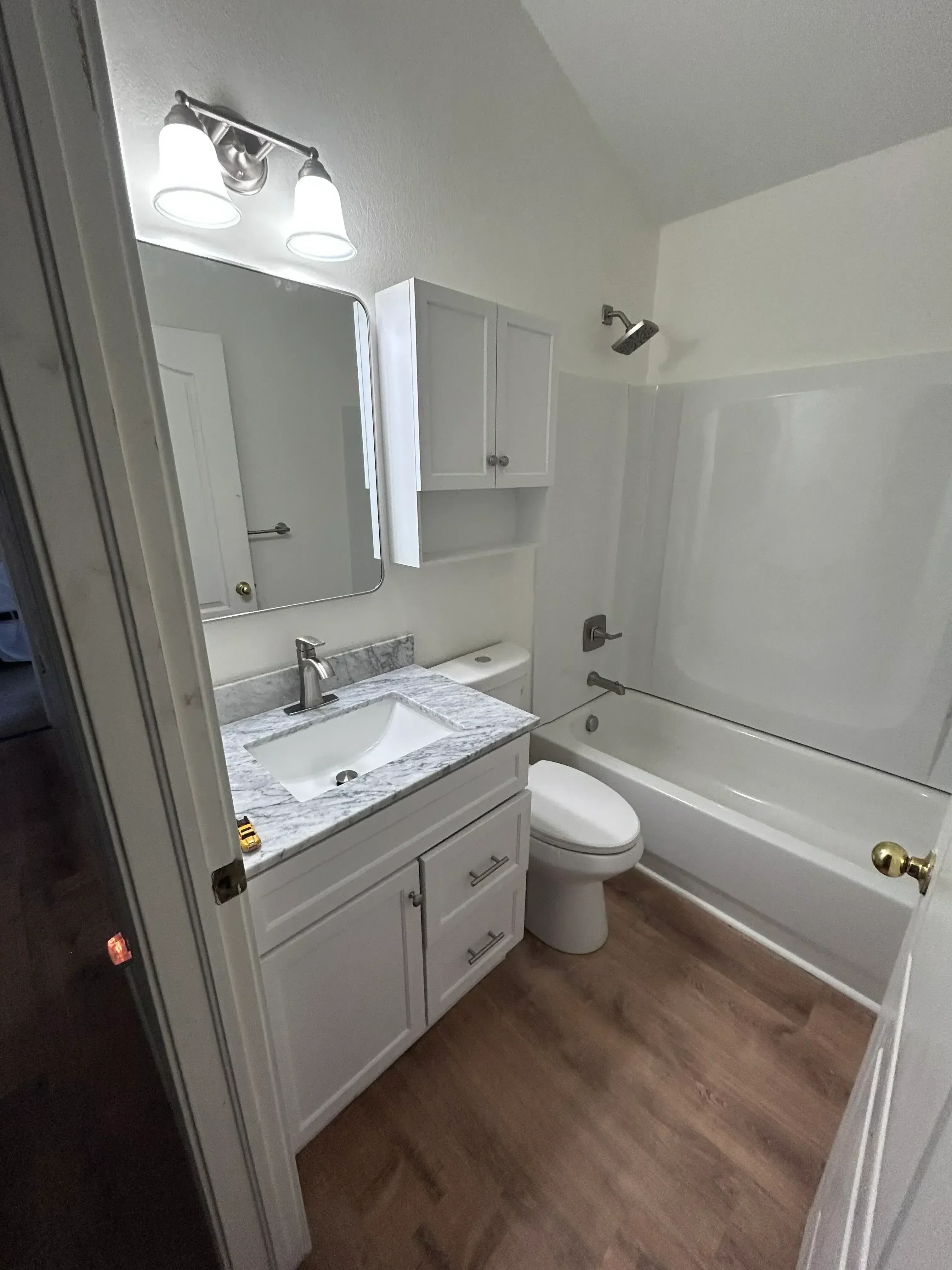 Bathroom with gray cabinetry, marble countertop, dual sinks, and wood-look vinyl flooring