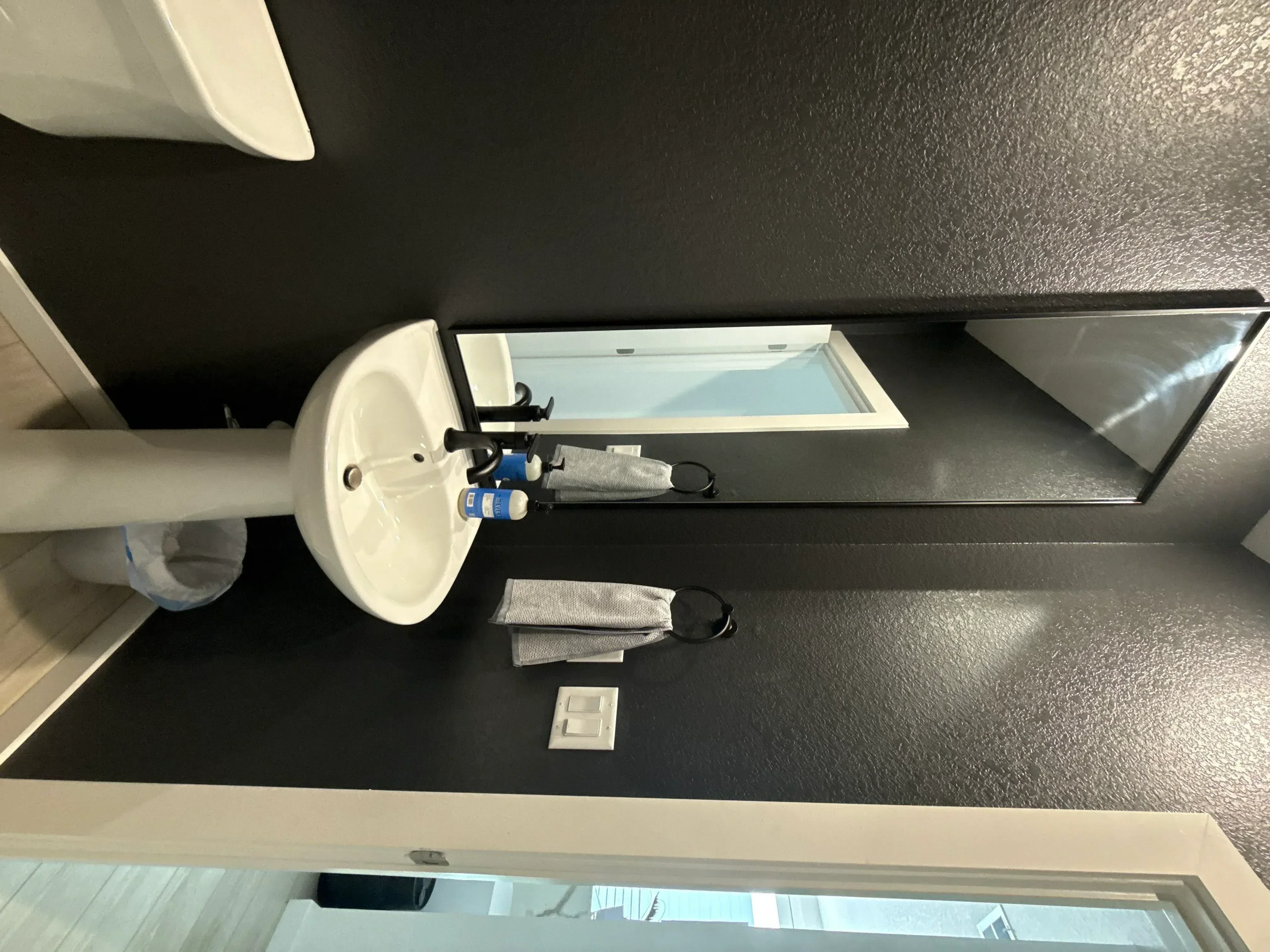 White ceramic sink with chrome faucet and large framed mirror installed on dark textured tile bathroom wall