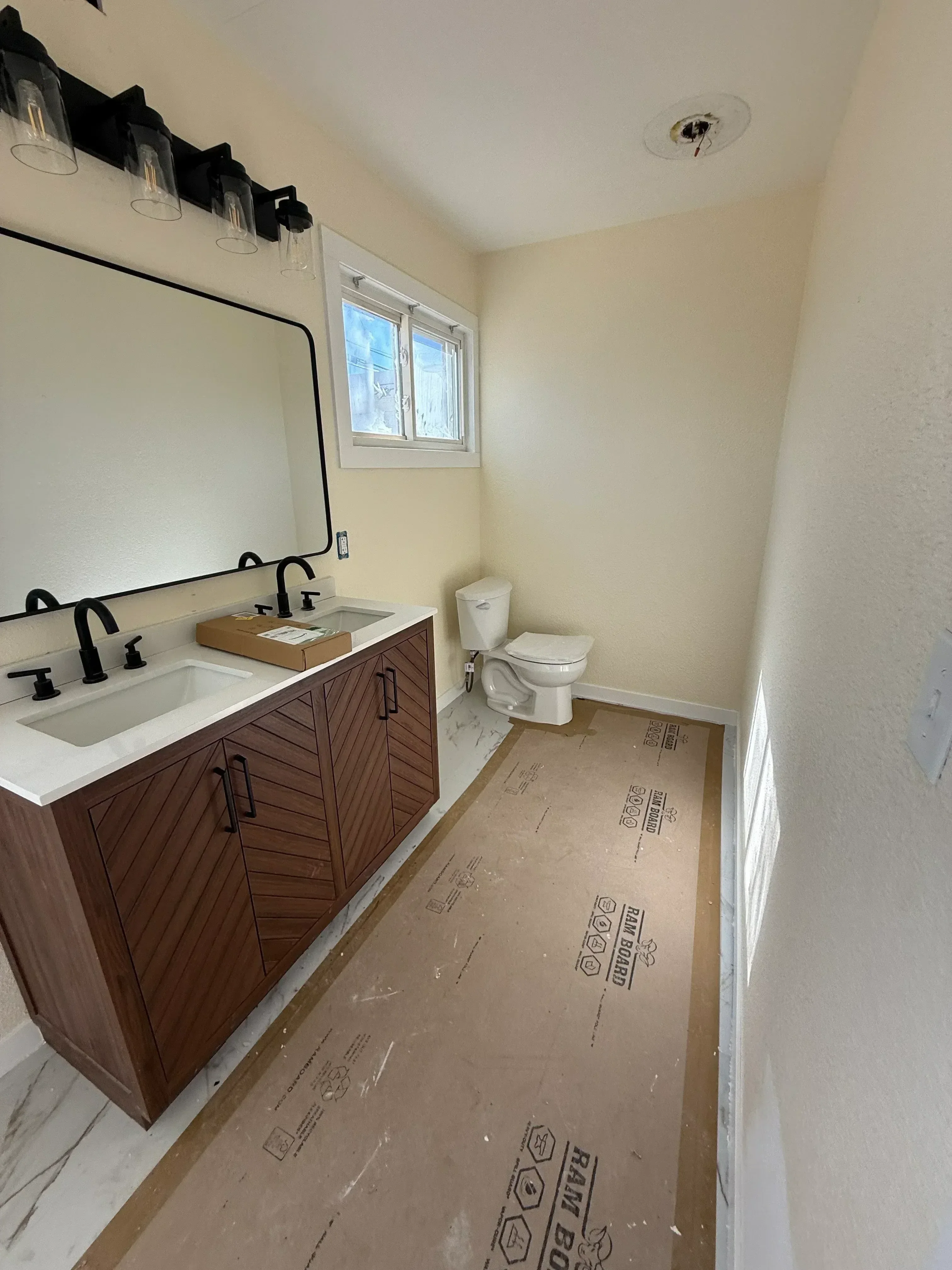 Bathroom renovation with dark wood vanity cabinetry, white drywall, and recessed lighting during construction