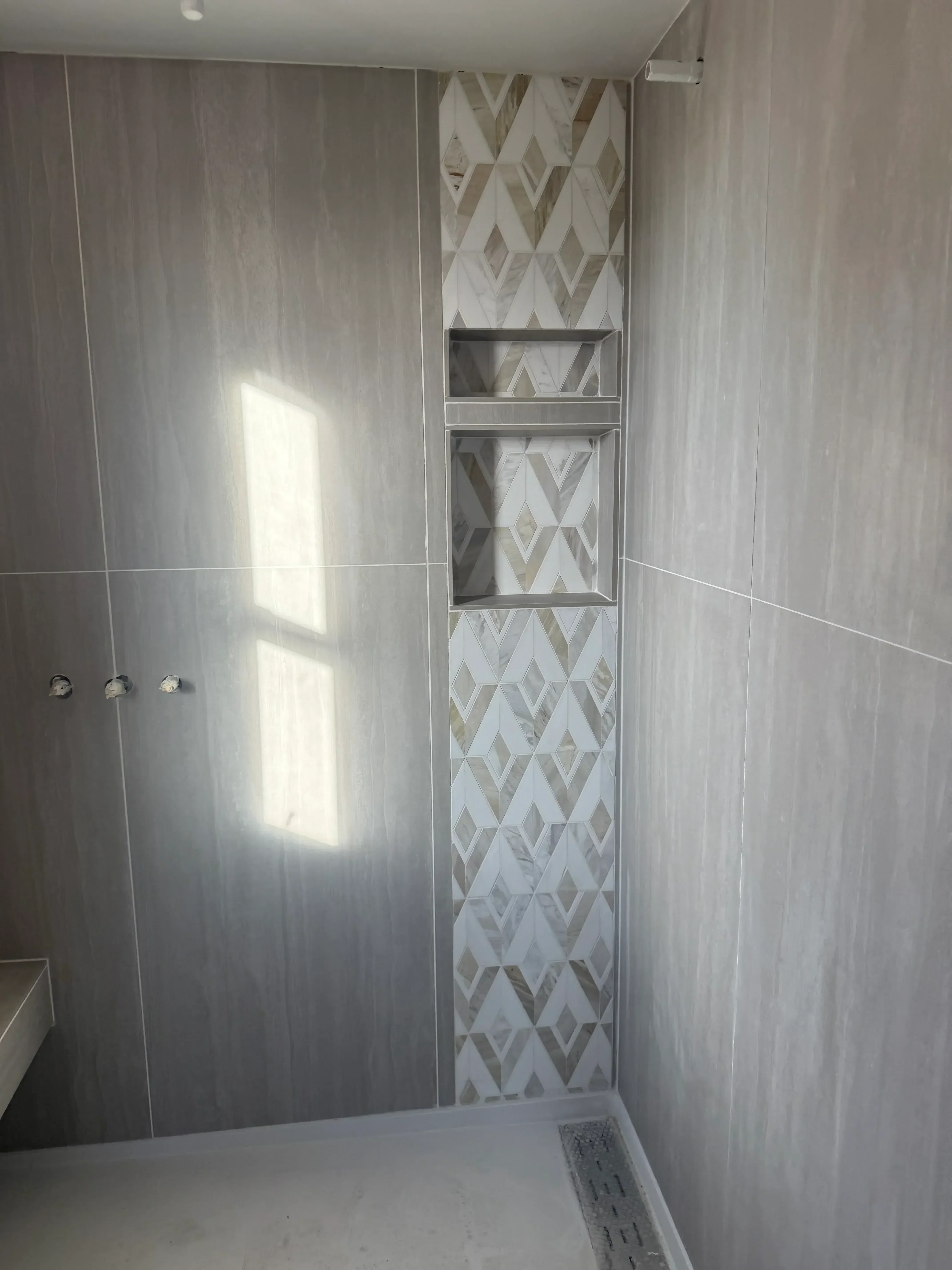 Frameless glass shower enclosure with geometric patterned tile accent wall and chrome fixtures