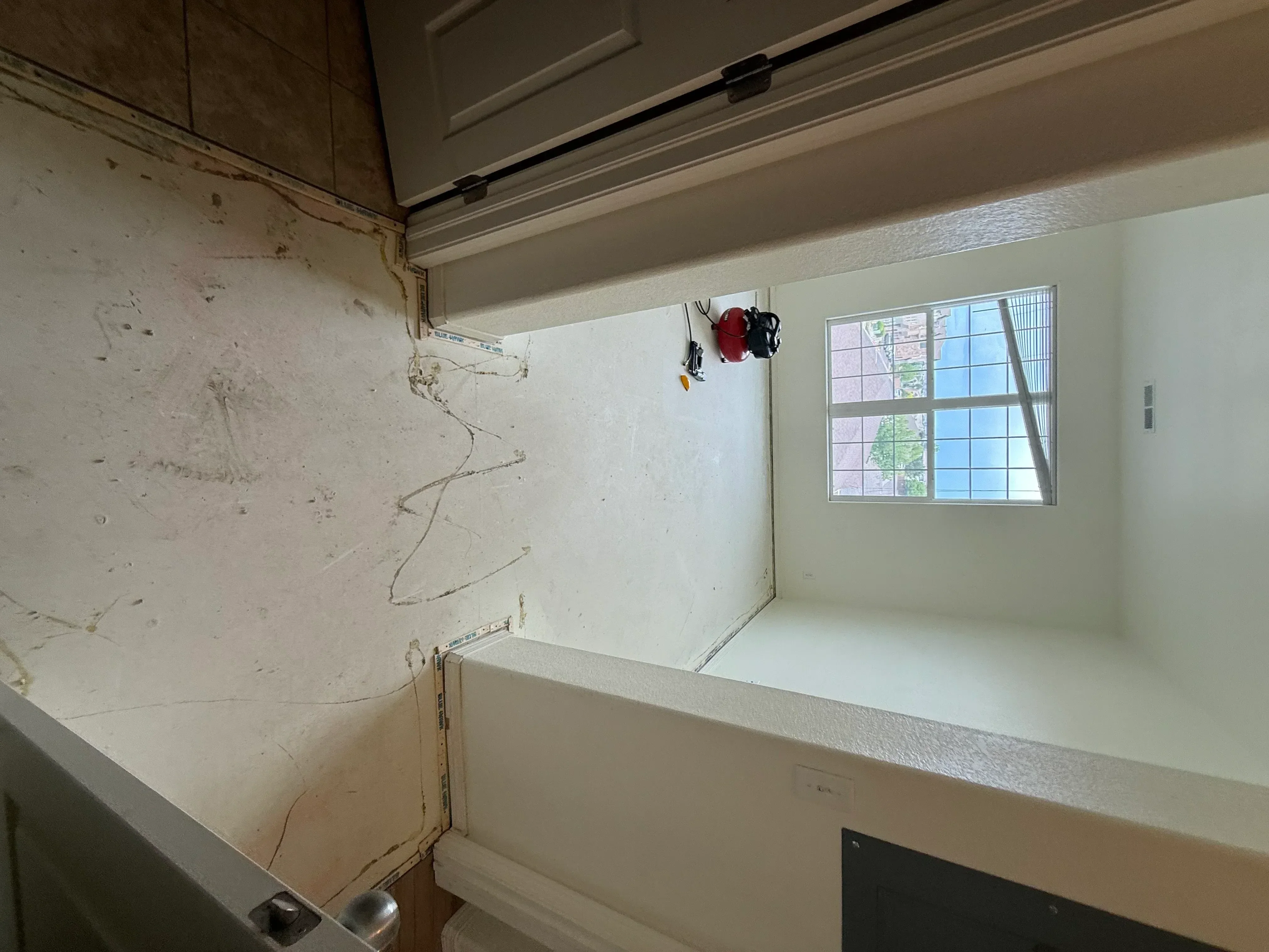 Kitchen window installation with drywall finishing, grid-pattern frame, and joint compound mudding
