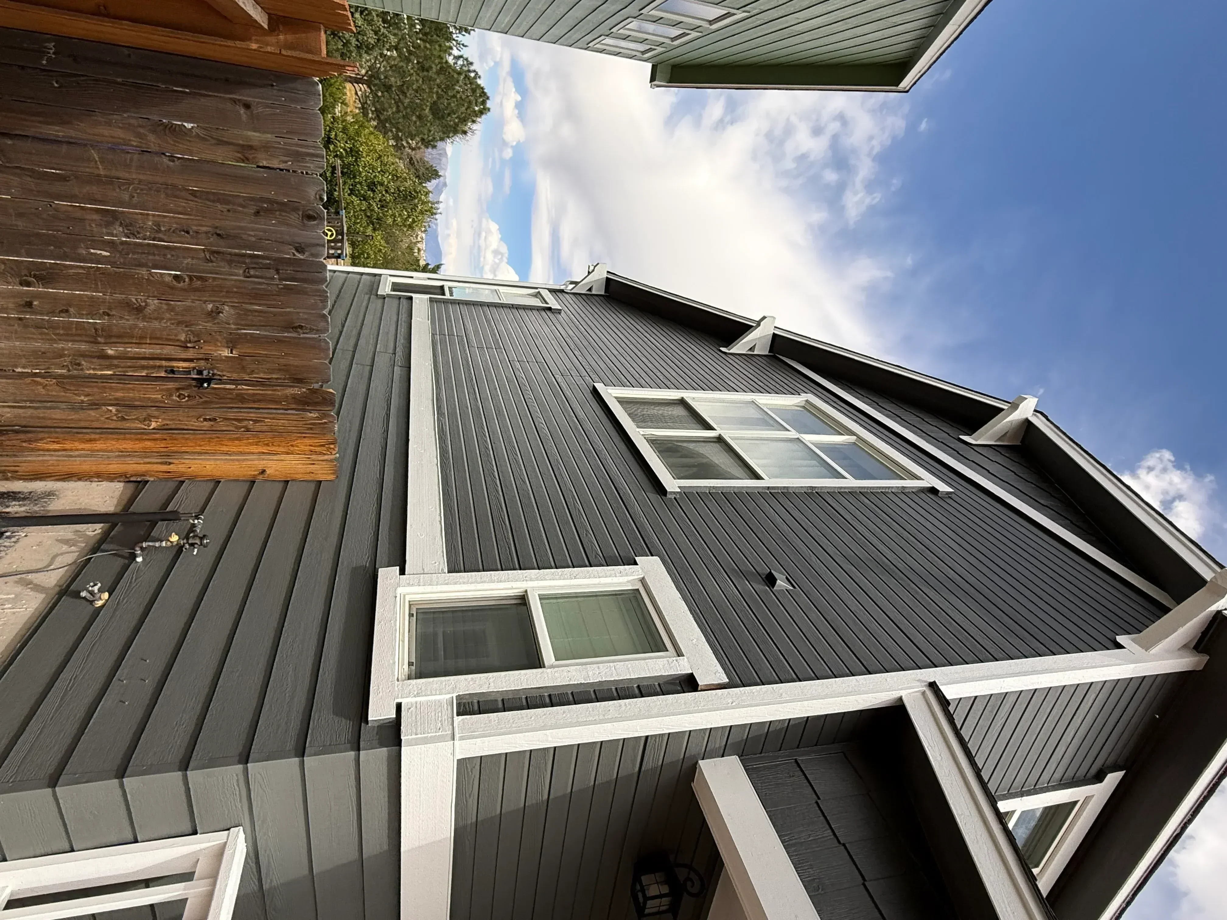 Charcoal gray vertical metal siding with white trim, windows, and soffit installation on residential exterior