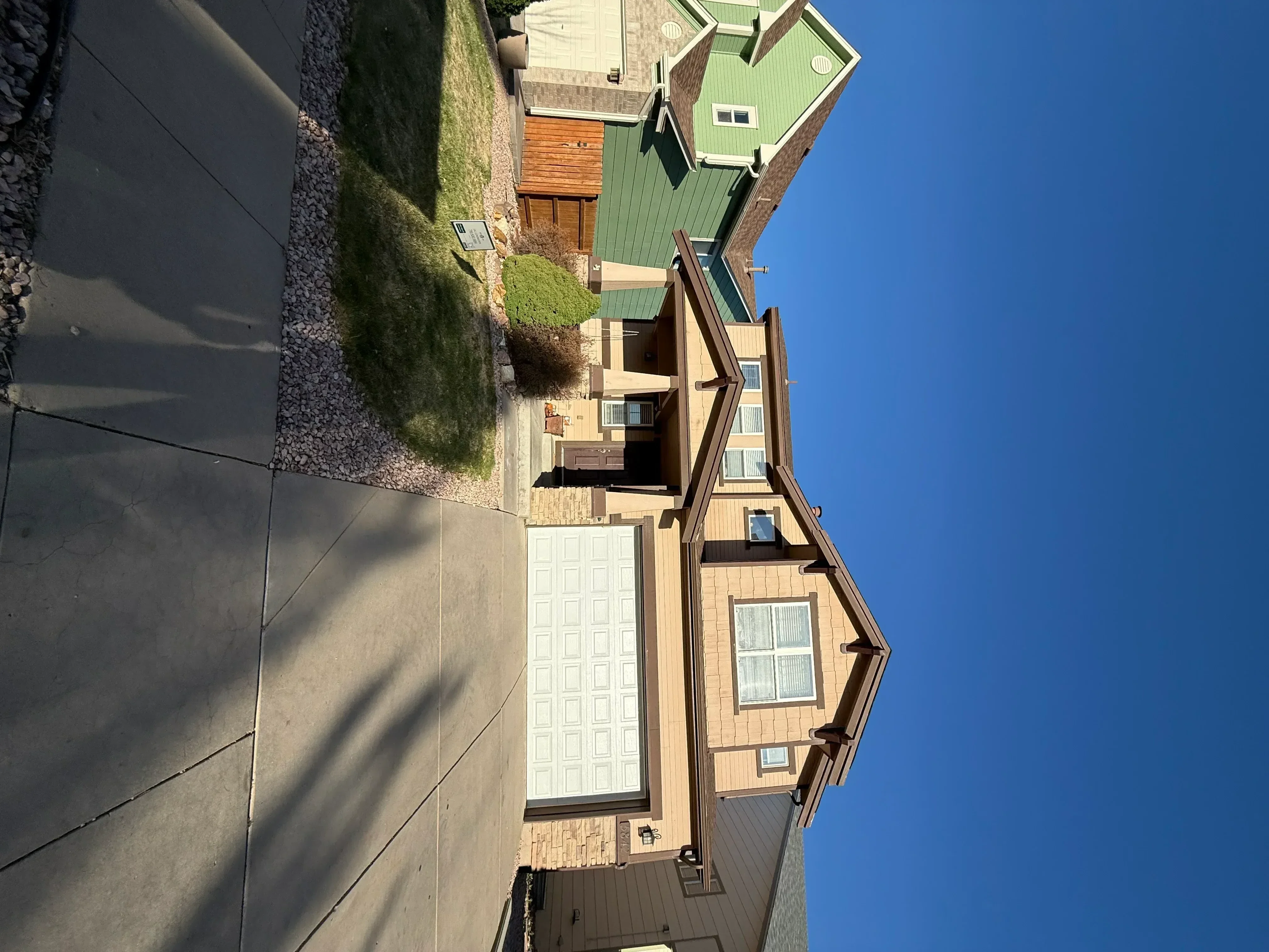 Tan fiber cement siding with brown trim, white garage door, and landscaped yard