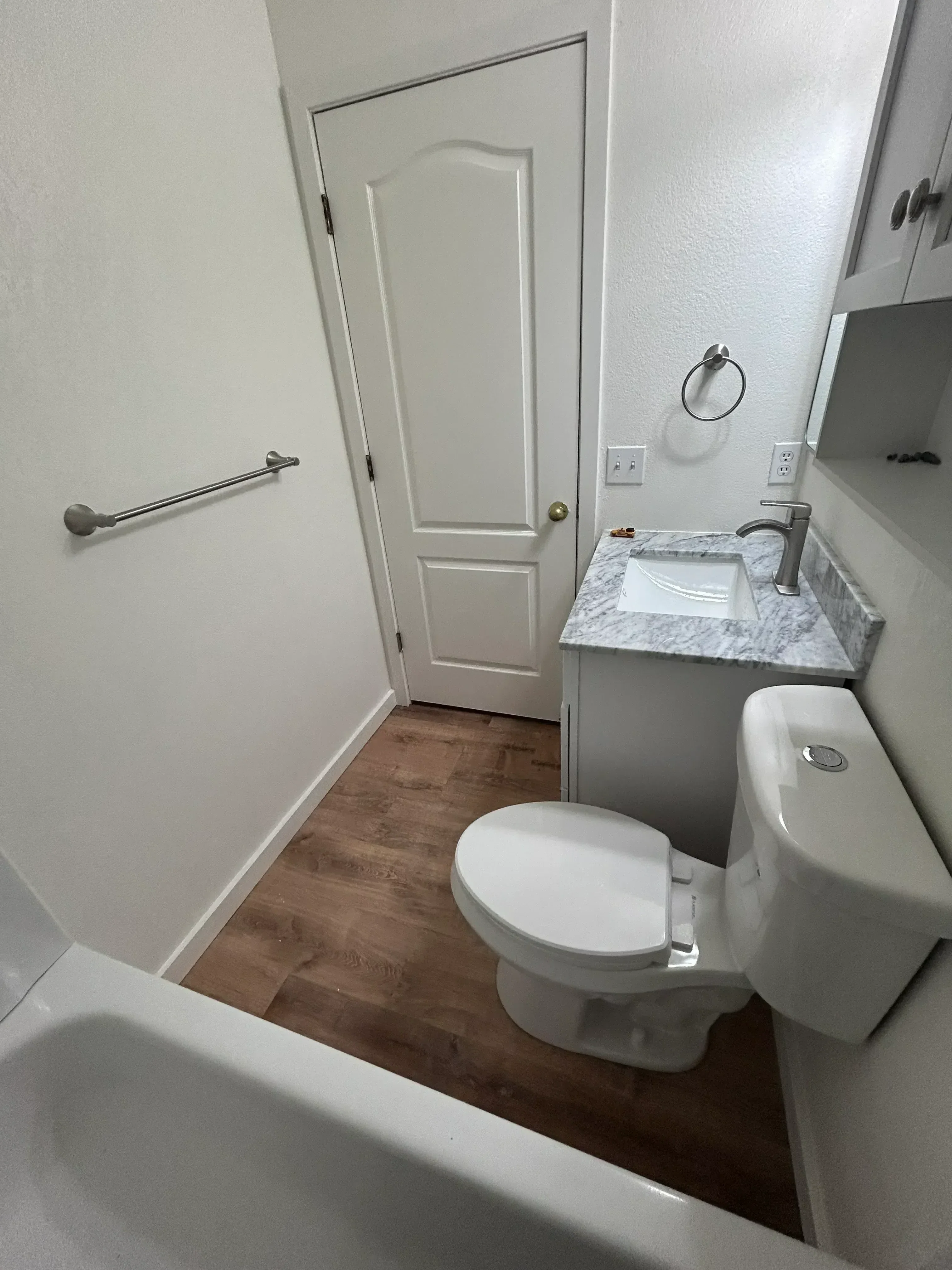 Bathroom with marble vanity, white cabinetry, wood-look vinyl flooring, and chrome fixtures