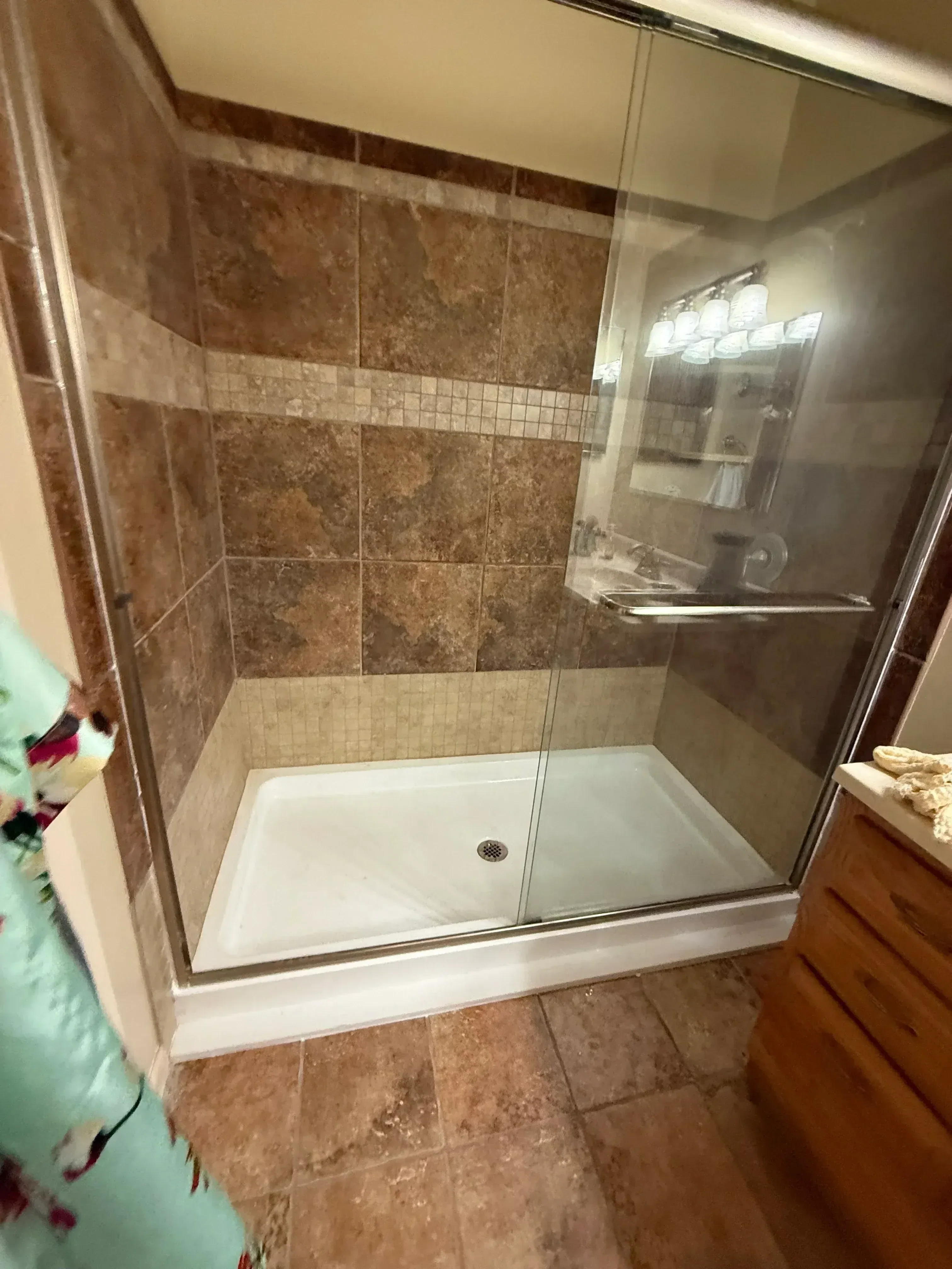 Walk-in shower with brown travertine tile, mosaic accents, and frameless glass enclosure doors
