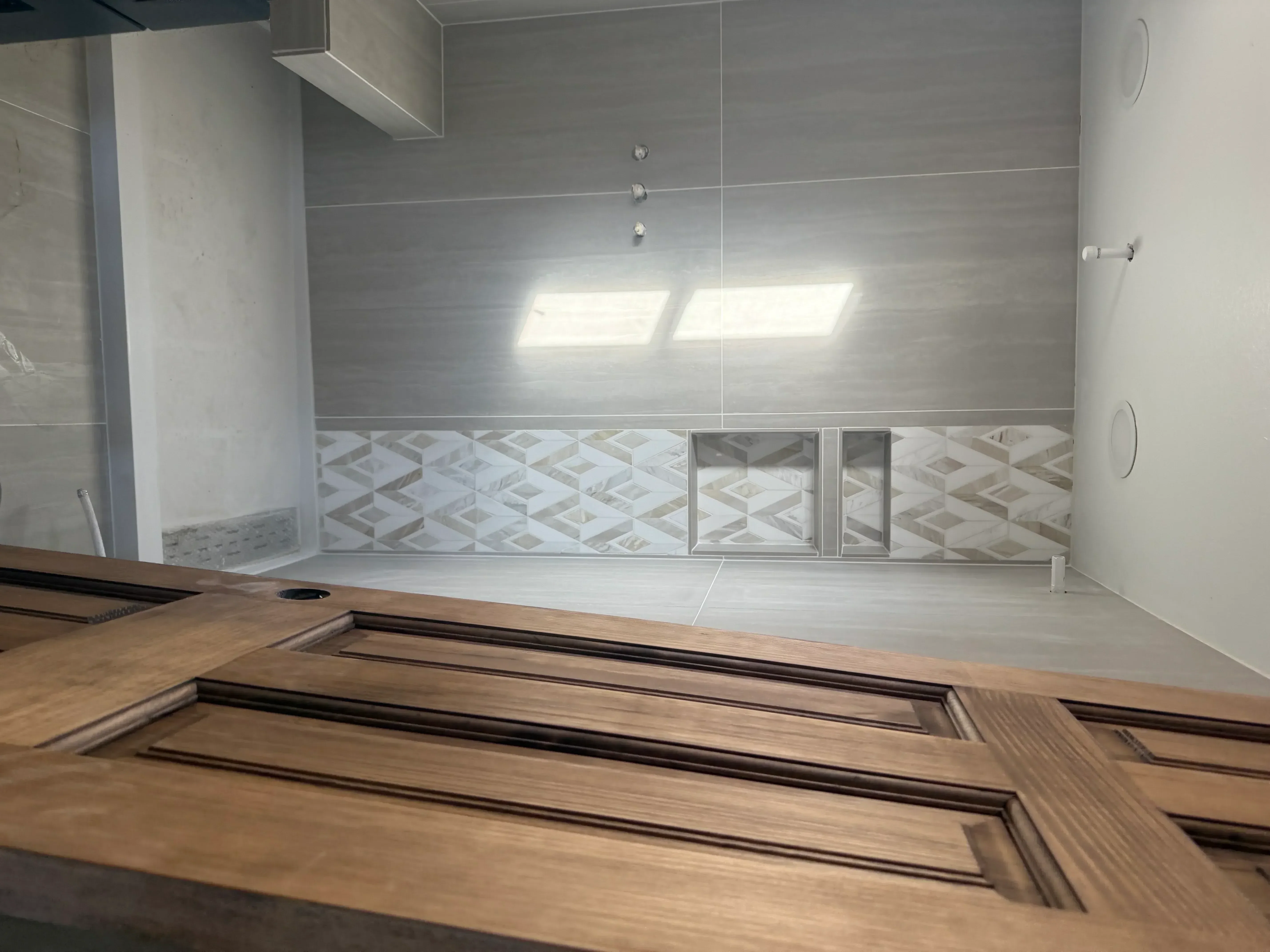 Walk-in shower with gray tile walls, geometric accent tile, frameless glass doors, and coffered wood ceiling